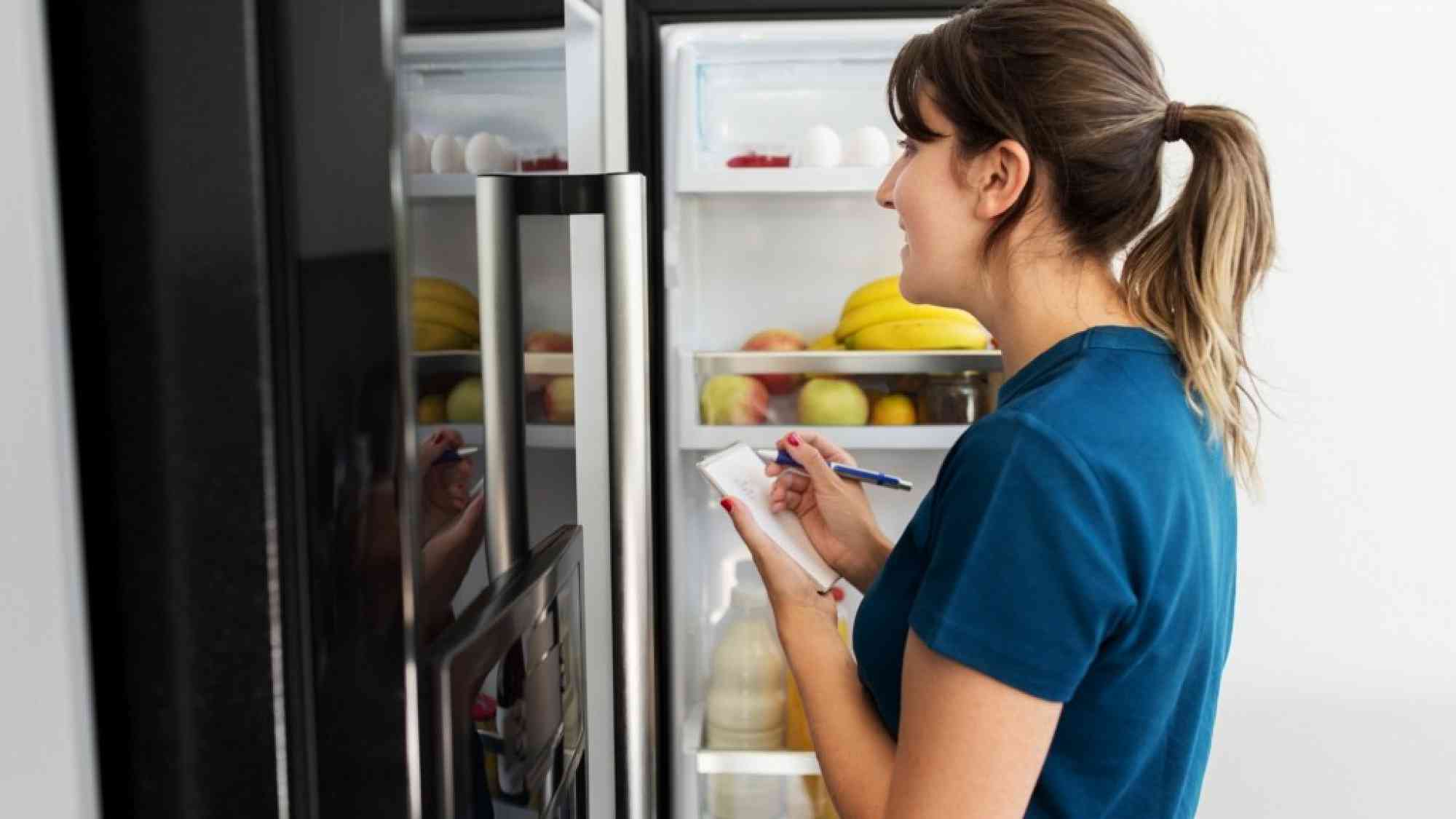 woman looking in freezer and making a list